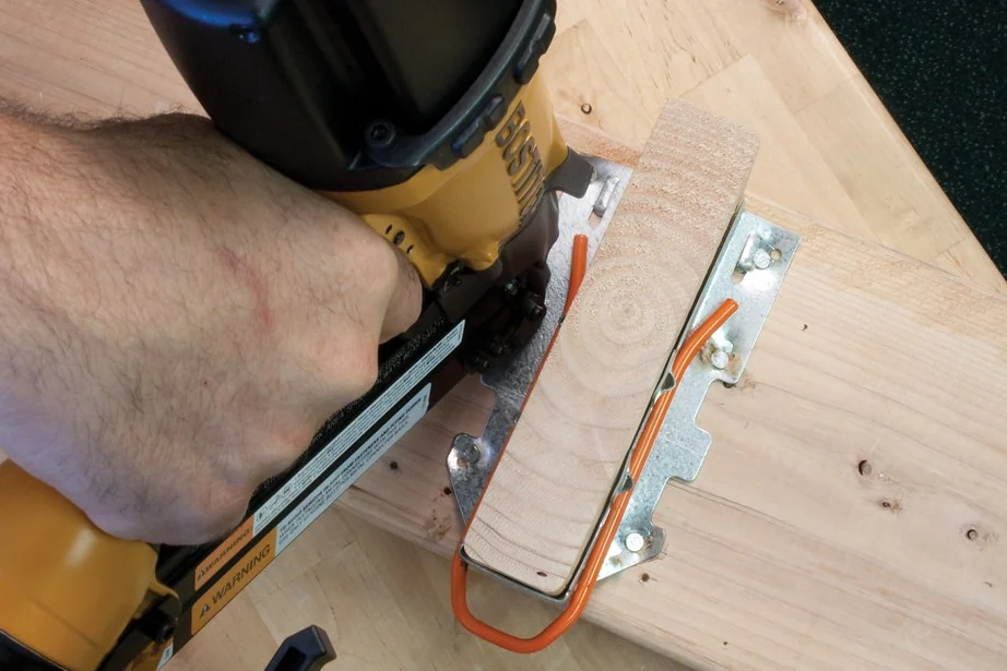Nail gun fixing a metal joist hanger to framing lumber