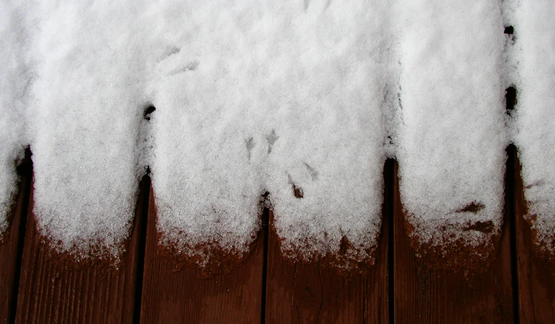 Snow lying across dark red deck boards